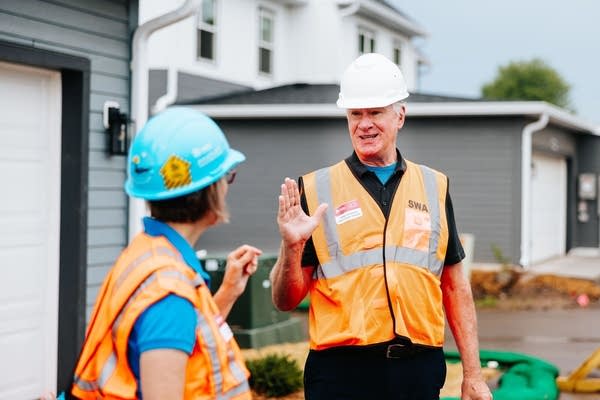 man in hard hat and orange vest talks with woman in hard hat 