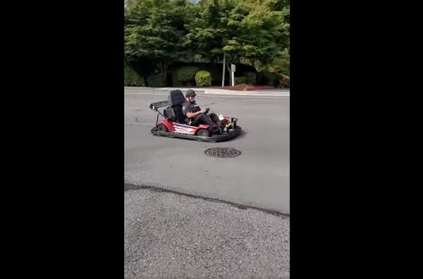 A police officer driving a go-kart down a wide, residential street