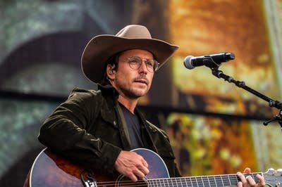 A man in a cowboy hat sings and plays guitar on a large outdoor stage