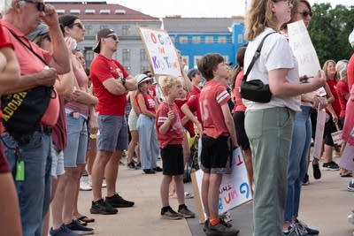 Children and adults wear red and hold signs at a protest.