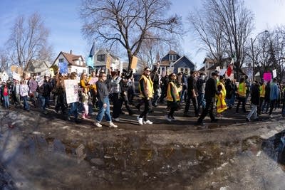 Wide-angle shot of a crowd marching down a residential street. Some wear hi-vis vests.