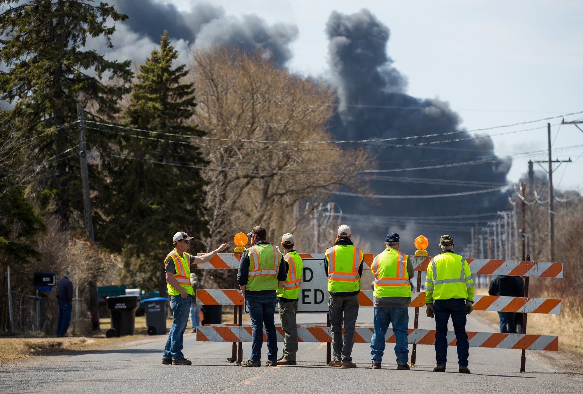 A group of onlookers watch a plume of black smoke billow.