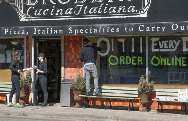 A person hands someone a box while standing outside a restaurant. 