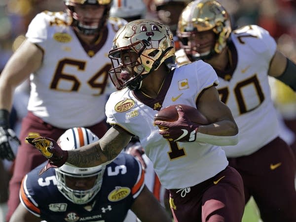 A football player holds up his hand, gripping the ball in his other arm.