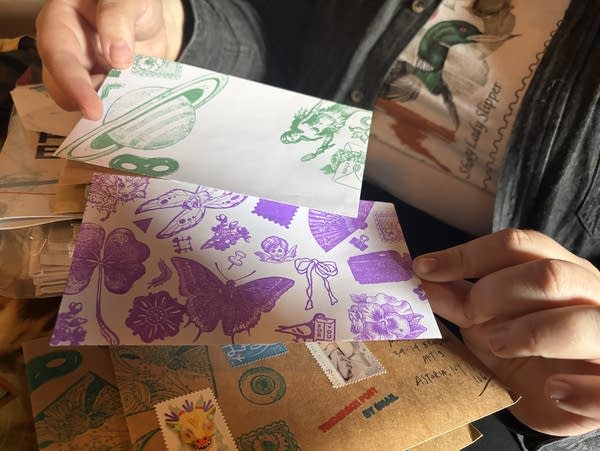 A person holds up two pieces of art sent in the mail.