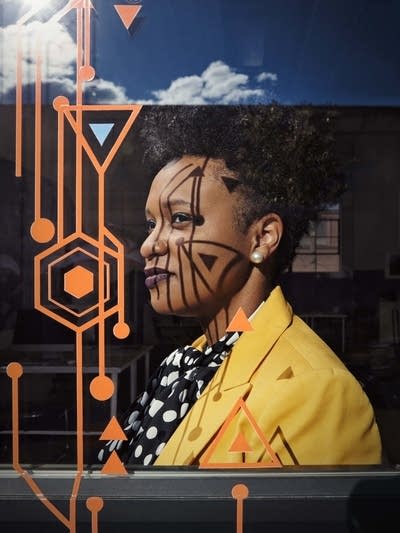 A woman stands next to a window.