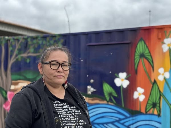A woman poses for a photo in front of a mural.