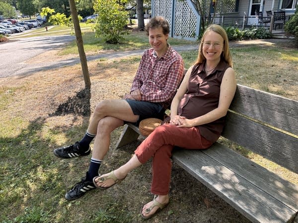 Two people sit on a park bench, smiling