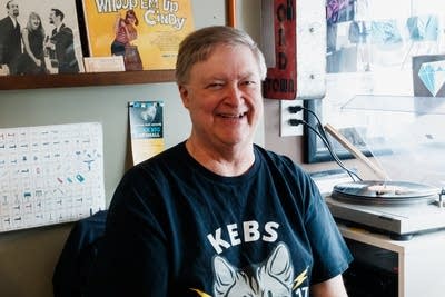 A person seated by a record turntable smiles for a photo