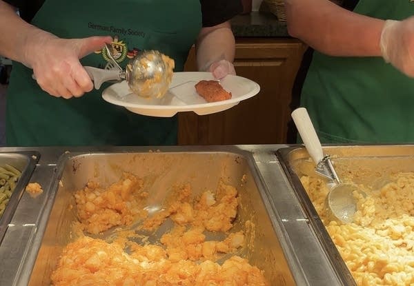A volunteer adds a heaping of macaroni and cheese next to the fried cod on a styrofoam plate.