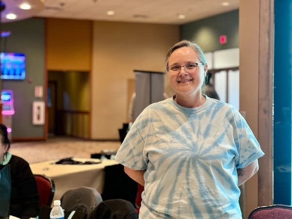A woman in a blue tie-dye shirt poses for a photo in a conference room.