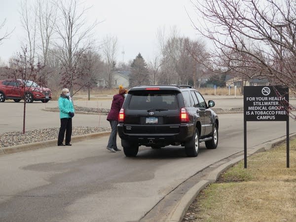 Two people with facemasks walk up to a car in a parking lot.