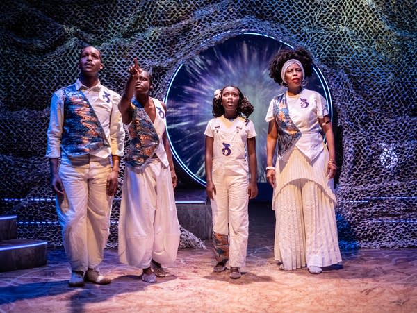 Four actors in flowing clothing on a futuristic theatrical set
