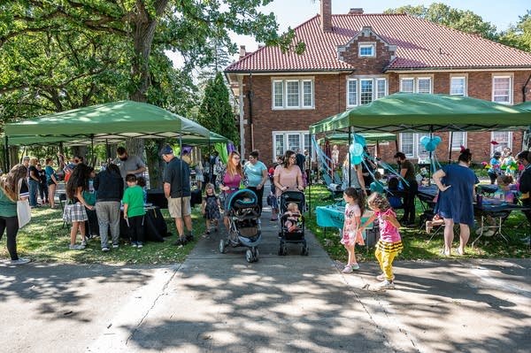 Families look at vendors under green tents on a lawn.