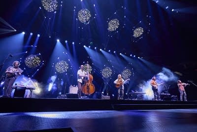 Five musicians play stringed instruments onstage in an arena