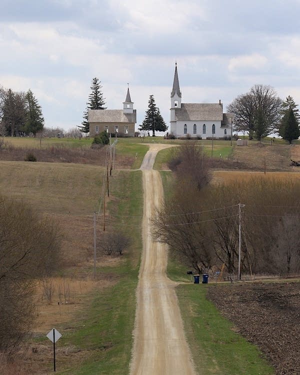 Two church buildings atop a hill at the end of a gravel road