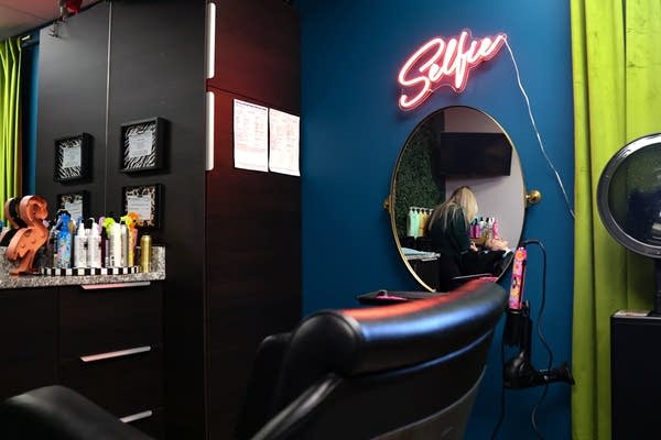 A stylist is seen washing a client's hair in a salon mirror.