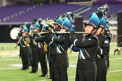A marching band performs on the field of a football stadium.