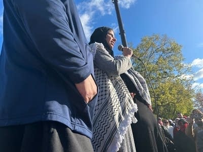 A woman speaks into a microphone in front of a crowd.