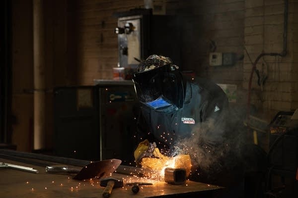 Sparks fly as Nick Bounds wears a welding mask and cuts a new key. 