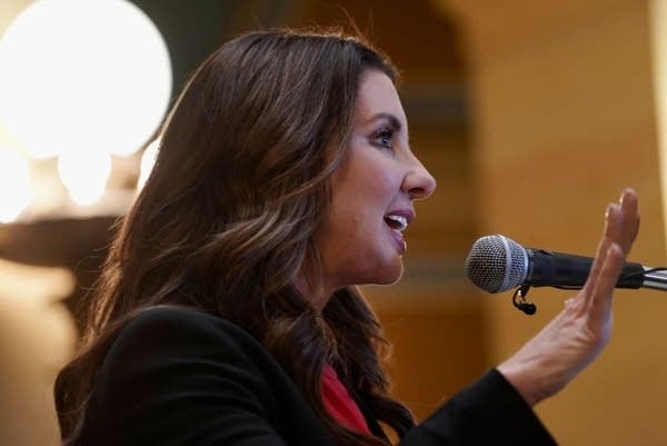 A woman raises her hand and speaks at a microphone