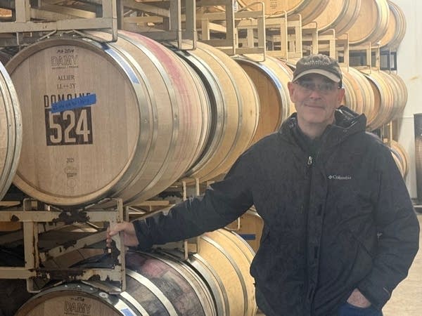 A man stands in front of wine barrels.