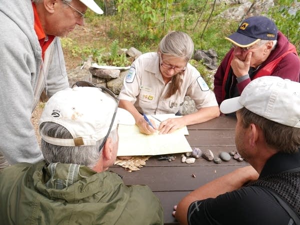 A woman points to a map as surrounding men observe.