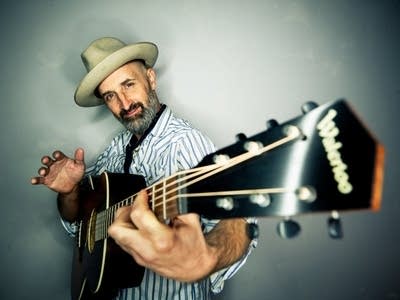 A man in a fedora looks down the neck of a guitar