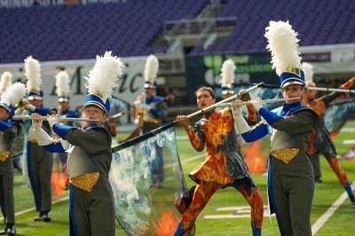 A marching band performs on the field of a football stadium.
