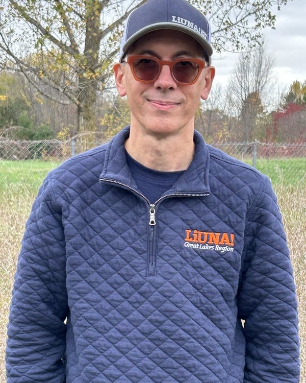 A man in a blue quilted quarter-zip and baseball cap.