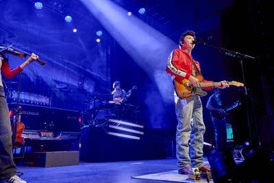 A musician sings and plays guitar onstage in a large music venue