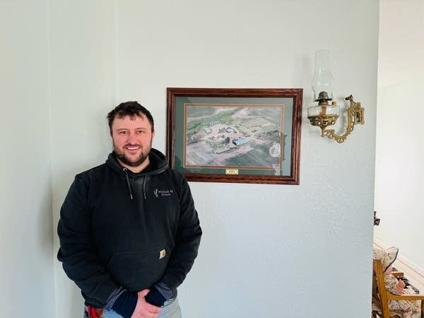 A man poses for a photo near a framed image on the wall.