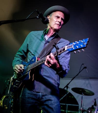 A man in a fedora plays guitar onstage