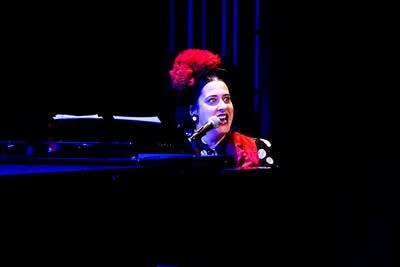 A musician sings and plays piano onstage in a theater