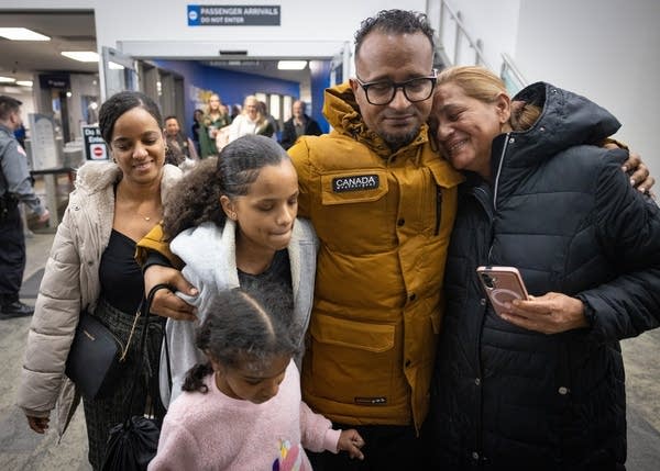 A man is embraced by his mother and two daughters. His wife stands next to him.