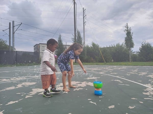 Two young people play with a bubble machine.