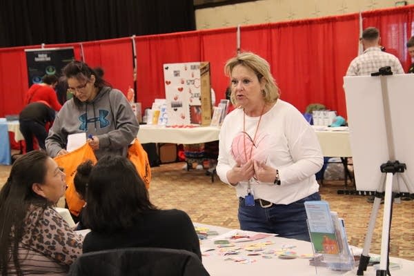 A woman speaks to people sitting at a table during a fair.
