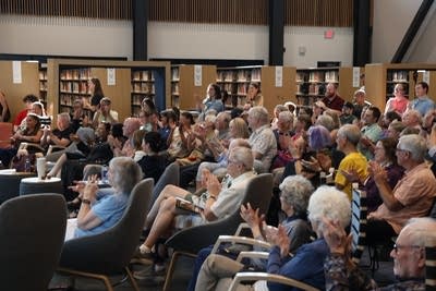 A crowd sits and listens in a large library setting.