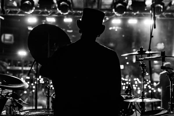 A man in a top hat plays drums on an outdoor stage