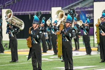 A marching band performs on the field of a football stadium.