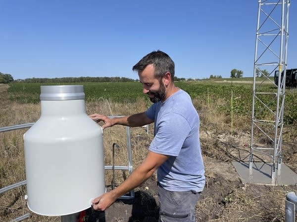 A man in a blue shirt works on building a weather data station in a farm field.
