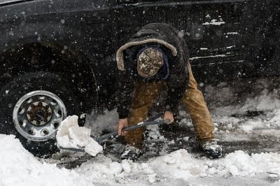 A man shovels snow from under his truck.