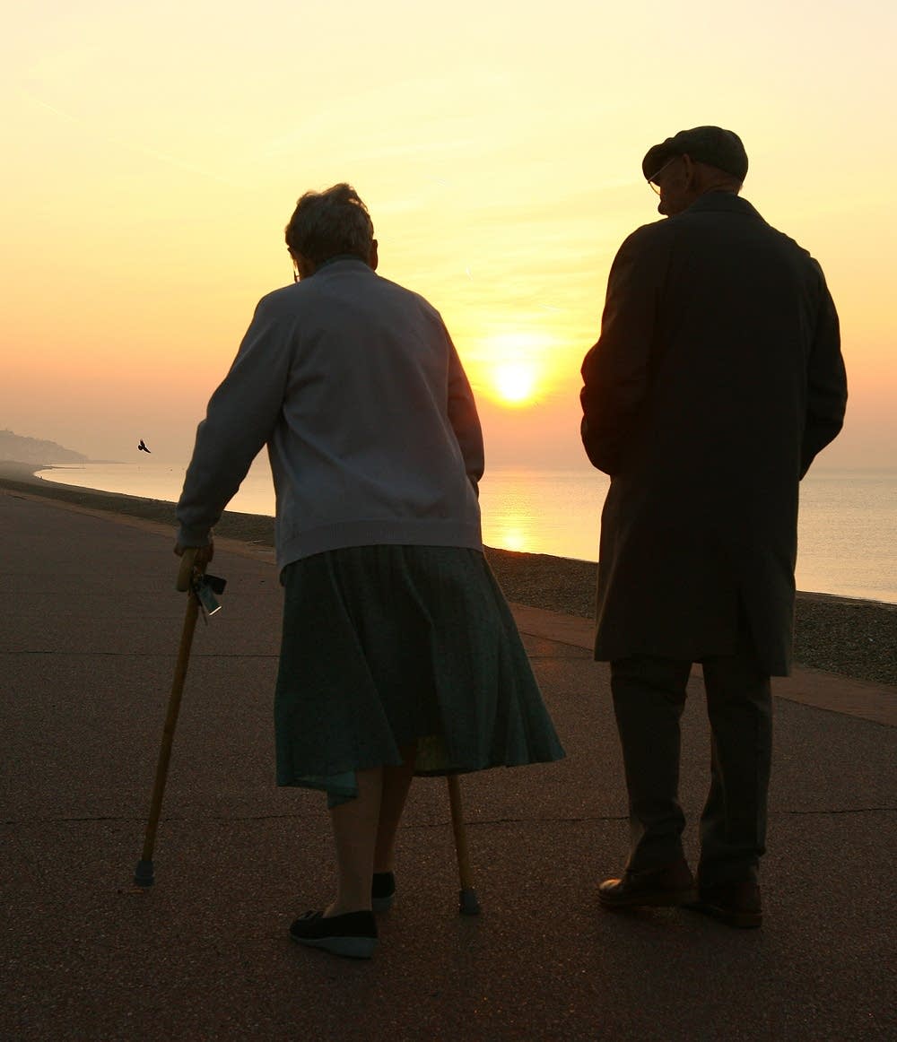 An elderly couple stroll on the sea front.