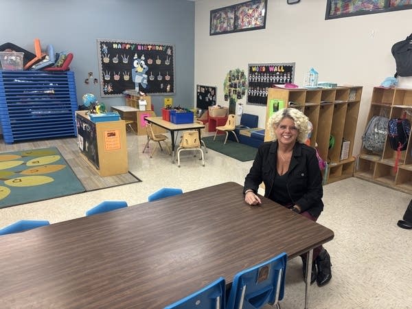A woman sits at a table in a classroom.