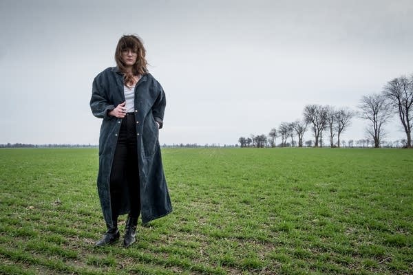 A woman in a long coat standing in a new-growth field