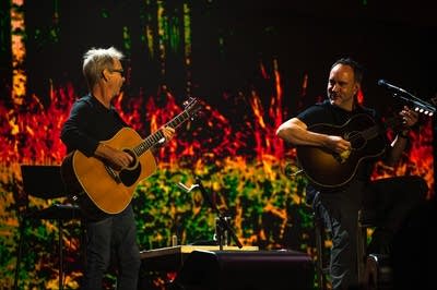 Two musicians play acoustic guitars on a large outdoor stage
