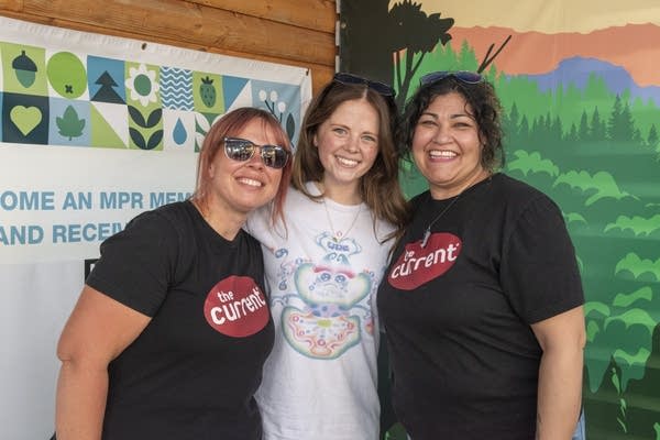 Three people pose for a photo together on an outdoor stage at a fair