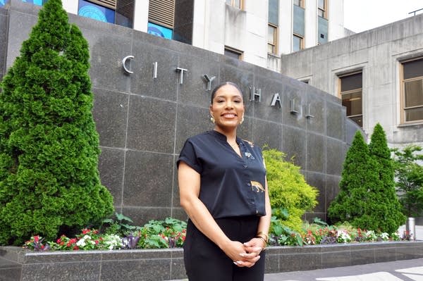 A Black woman in workwear poses in front of a wall that says City Hall