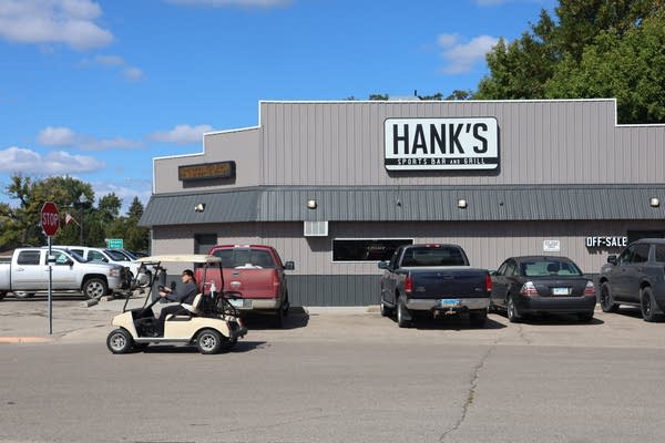 Several trucks and a golf cart are parked in front of a bar named Hank's.