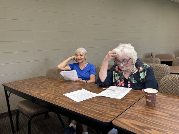 Two women sit at a table looking over papers.